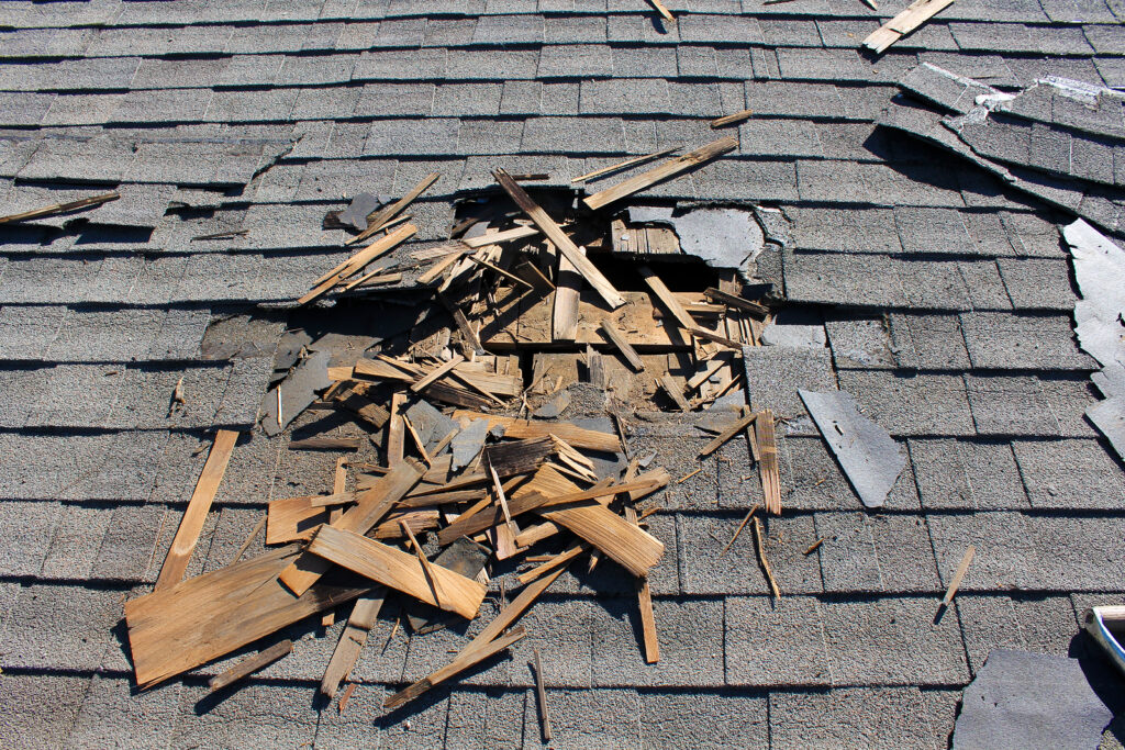 Up close of a roof that had suffered extensive damage, creating a hold in the asphalt shingles.